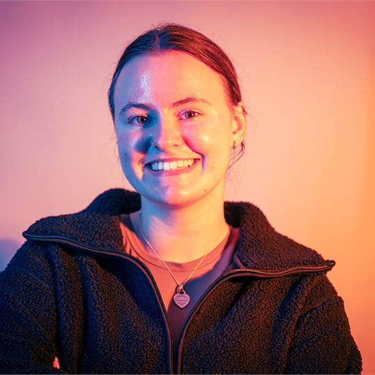 Student smiling at the camera, lit up by neon orange lights