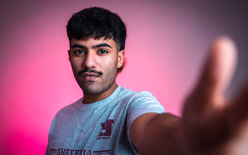 Student wearing a Hallam Varsity t-shirt and glasses, smiling at the camera.