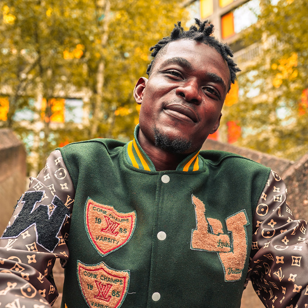 A student wearing a green varsity jacket confidently smiling at the camera.