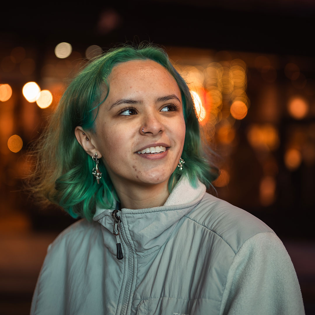 A student with green hair smiling and looking into the distance