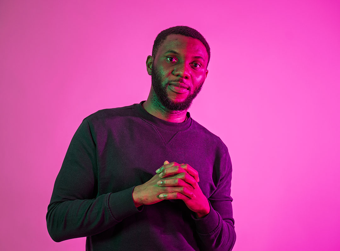 Student with their hands clasped looking towards the camera with a neutral expression.