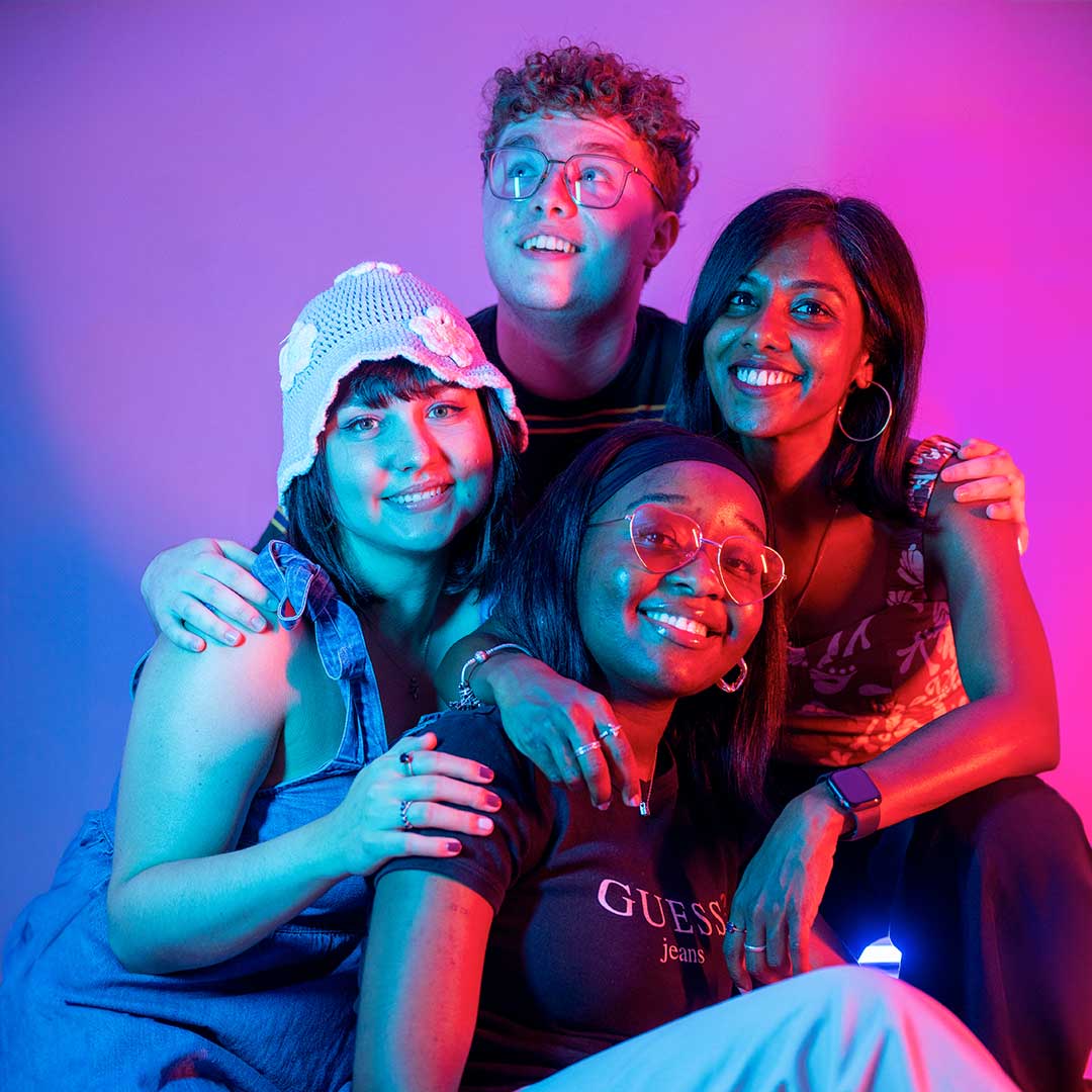 Four students sat with their arms around each other smiling and laughing