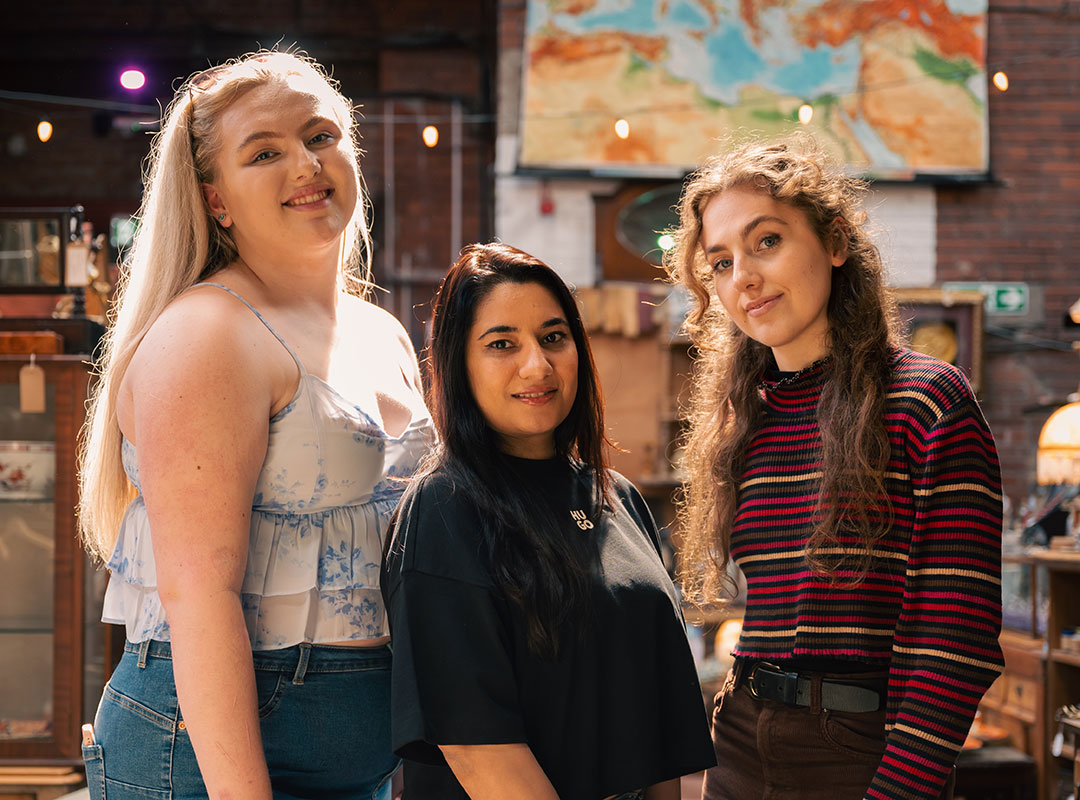 HSU Officers Abi, Shafaq, and Molly standing indoors with a map on the wall in the background. They are smiling and casually dressed.