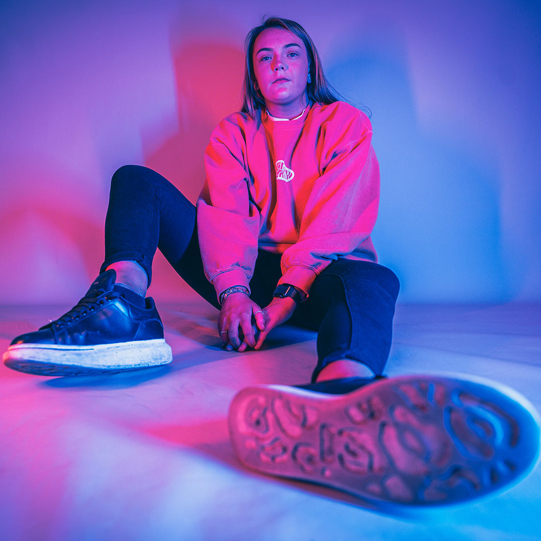 A student sat on floor with bent legs, lit up by neon lights