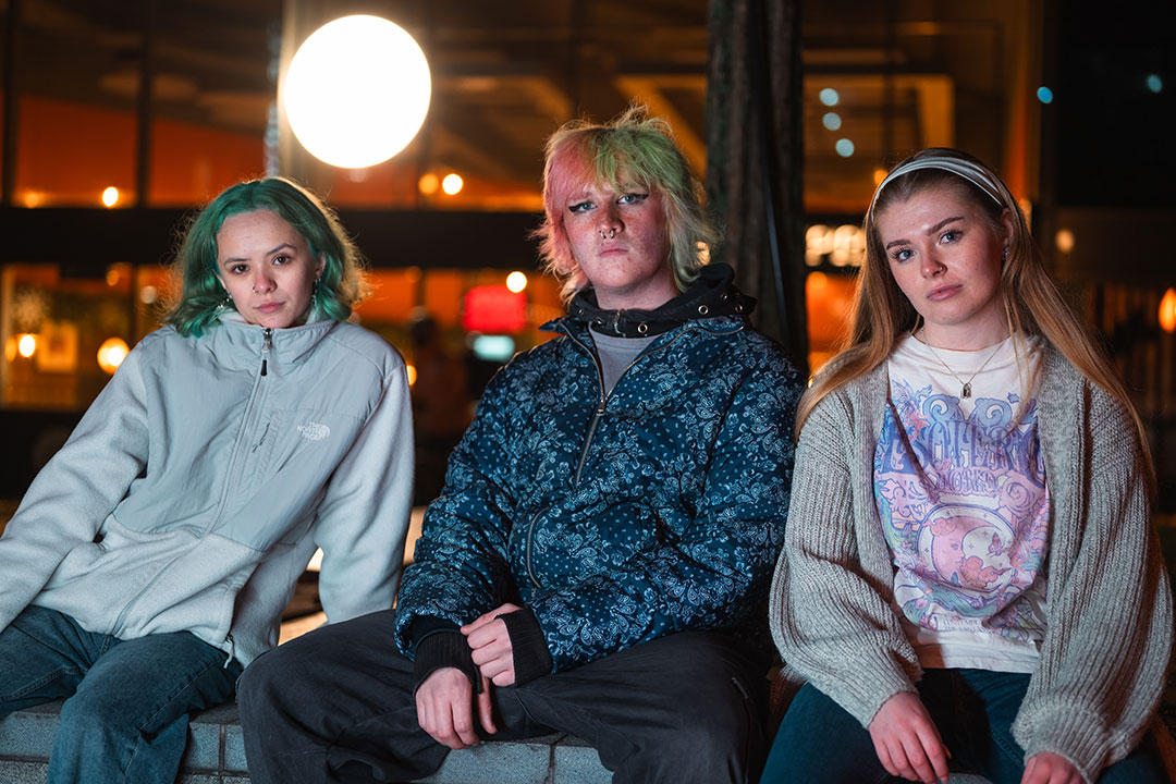 Three students sat on a wall at night staring at the camera