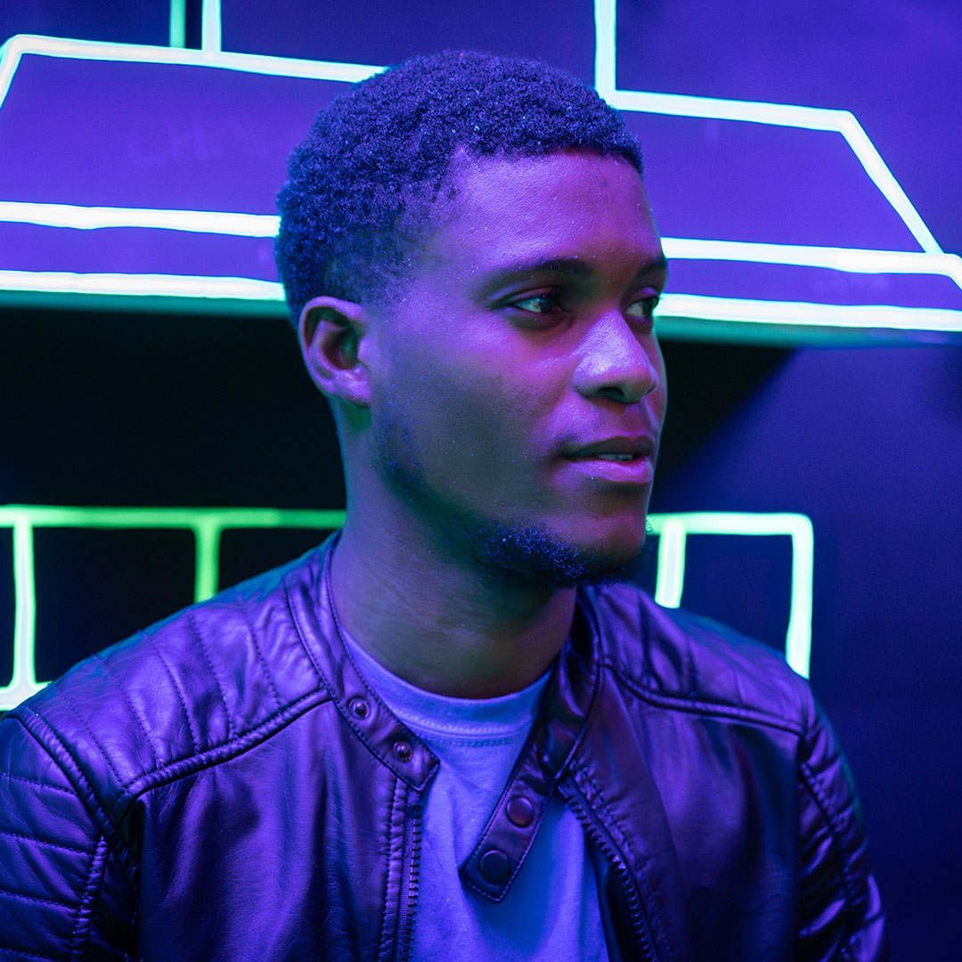 A Black student stood leaning against a wall with leon lighting behind him