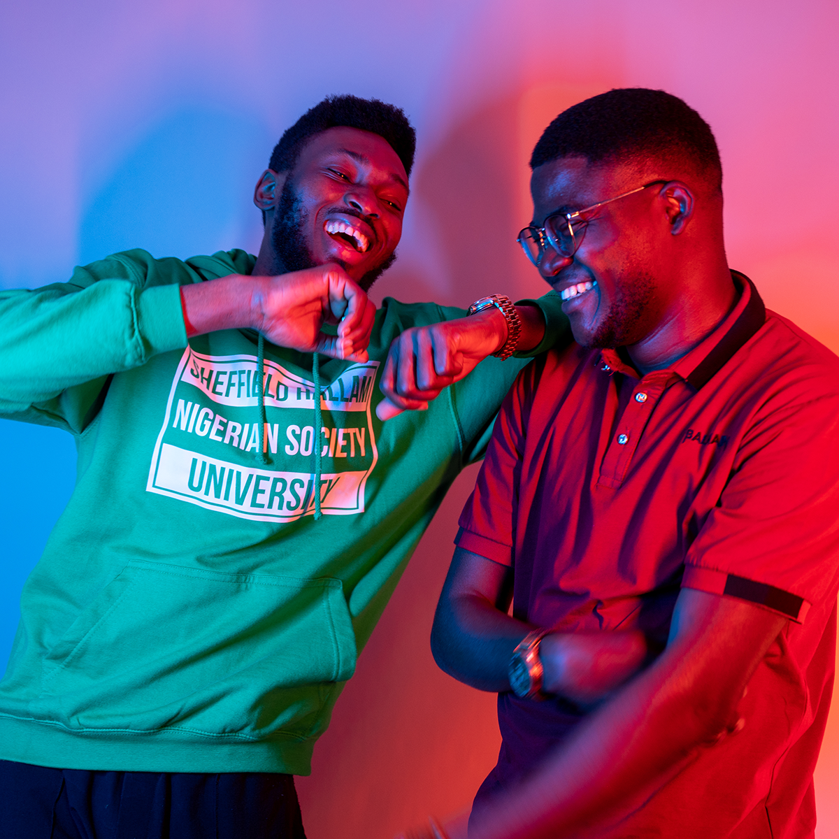 Two students laughing, they're illuminated by neon pink and purple lights