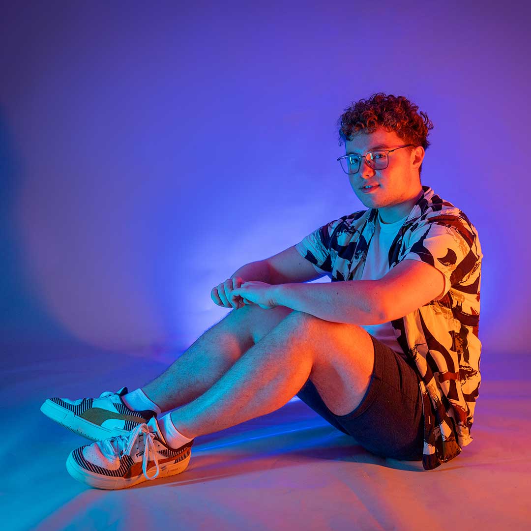 Four students sat on the floor looking at the camera, lit up by neon pink lights