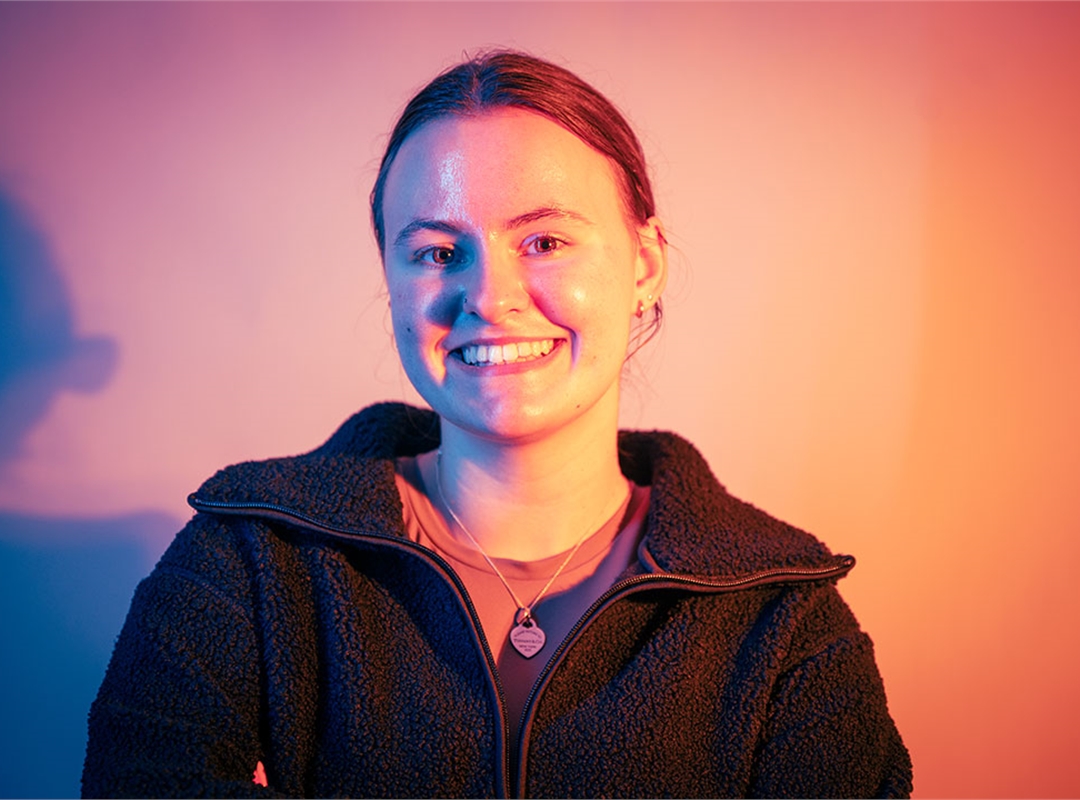Student smiling at the camera, lit up by neon orange lights