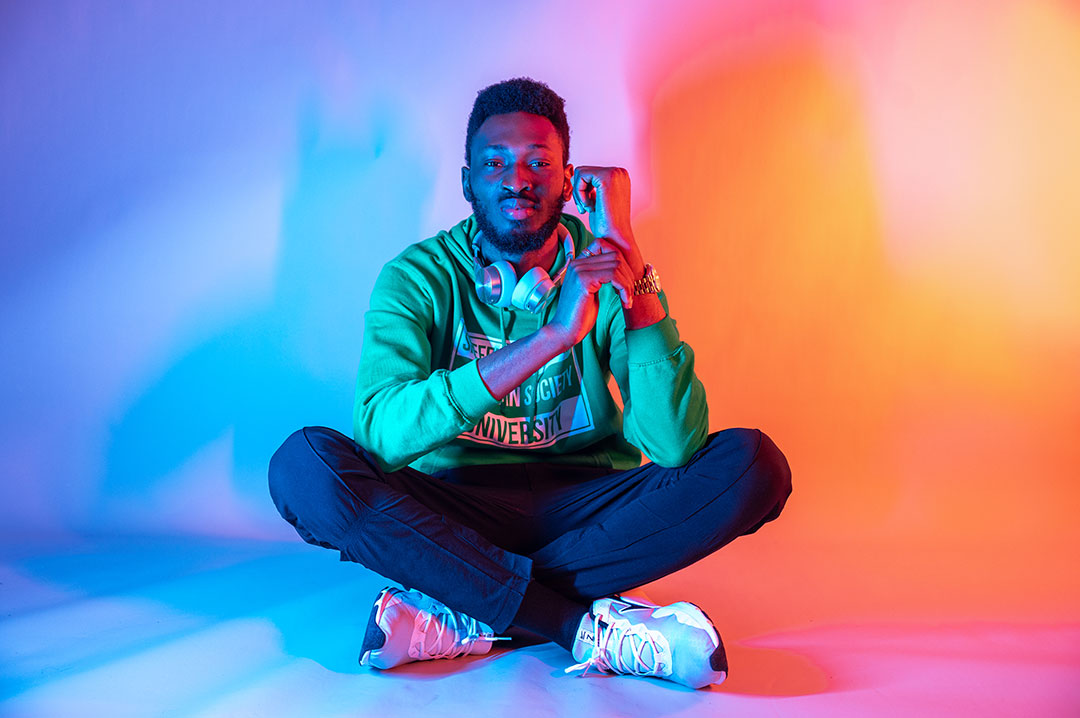 Student lit with blue and orange lights while sat with legs crossed and their head leaning on their hand.