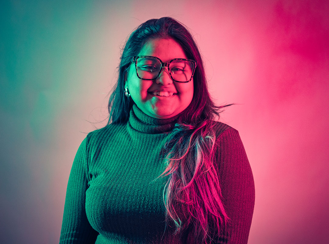 Student smiling at the camera while lit up by teal and pink neon lights.
