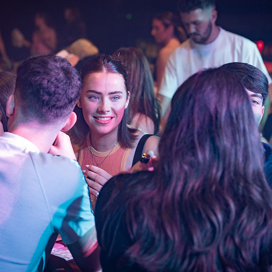 Student smiling at a friend while sat on a night out.