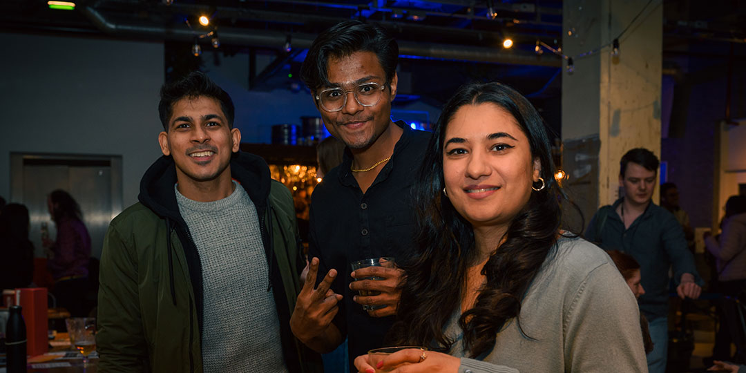Shafaq, HSU International Students' Officer 2024/25, holding a drink and smiling at the camera with two other students. One of the students is making a peace sign with their fingers.