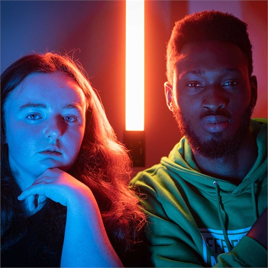 Two students staring into the camera, lit up by blue and red lights all around them