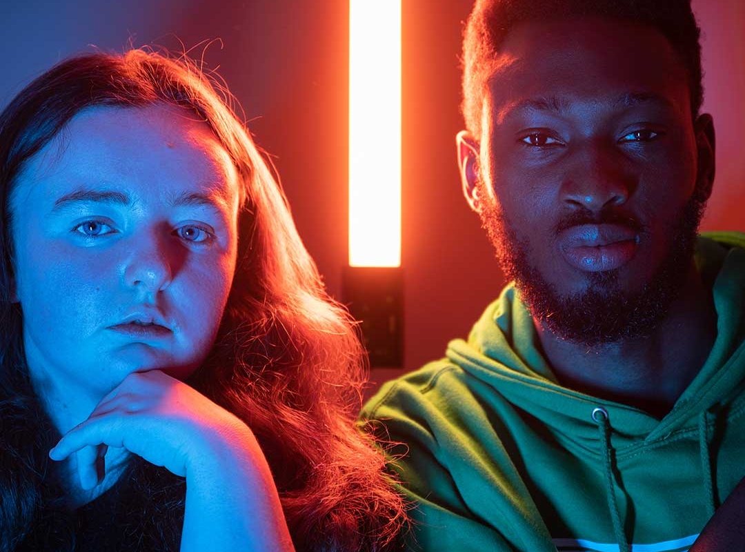 Two students staring into the camera, lit up by blue and red lights all around them