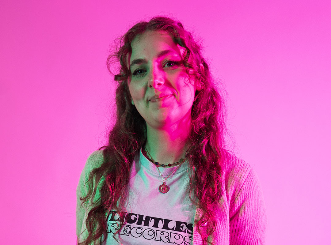 Student smiling at the camera and lit with bright pink lights.