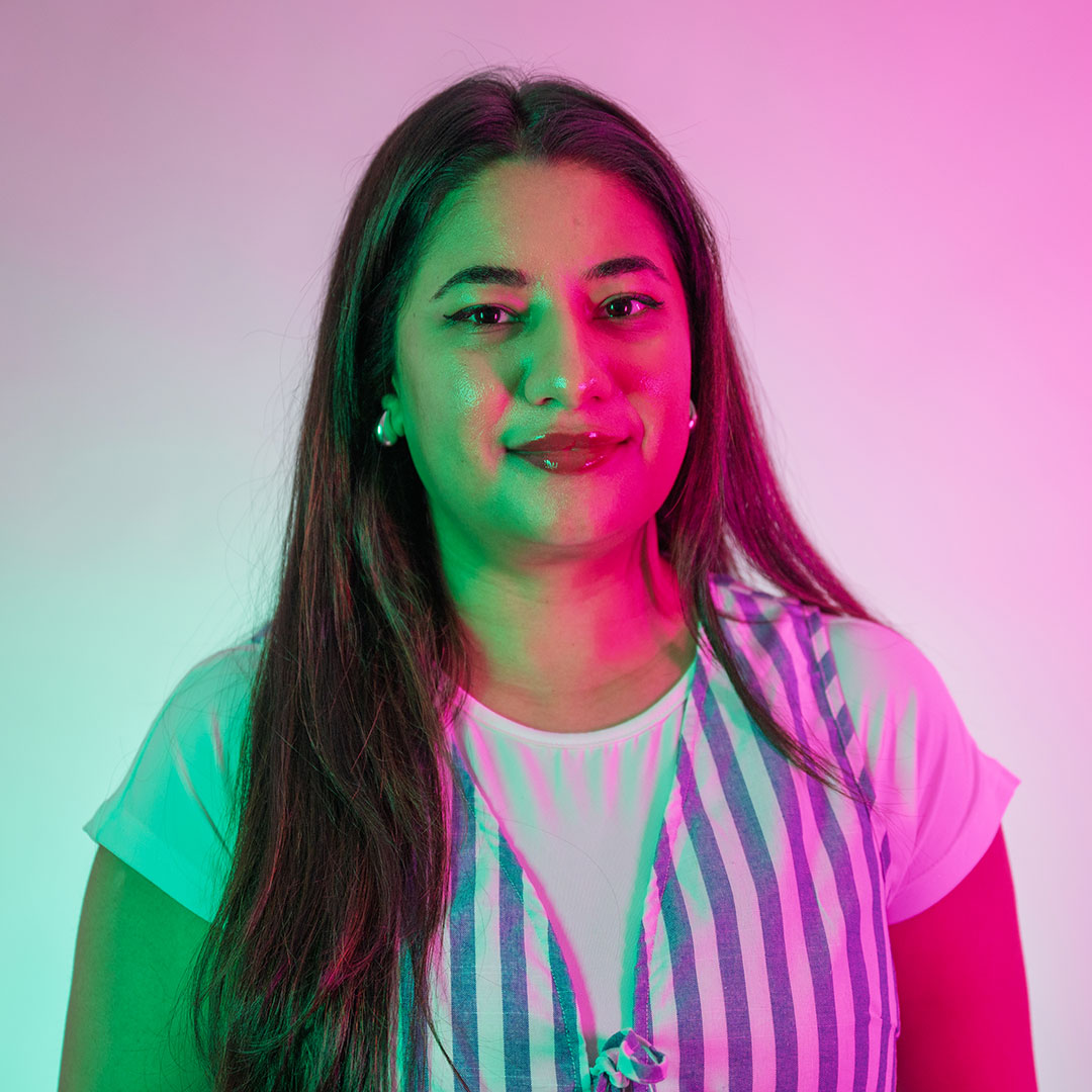 Shafaq Sajid smiling at the camera and lit by bright green and pink lights.