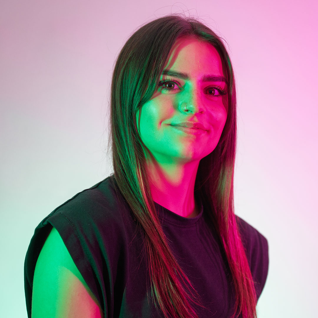 Leah Steel smiling at the camera and lit by bright green and pink lights.