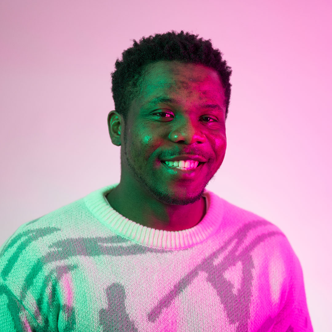 Franklin Okafor smiling at the camera and lit by bright green and pink lights.
