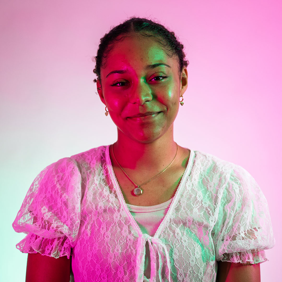 Layla Barrett smiling at the camera and lit by bright green and pink lights.