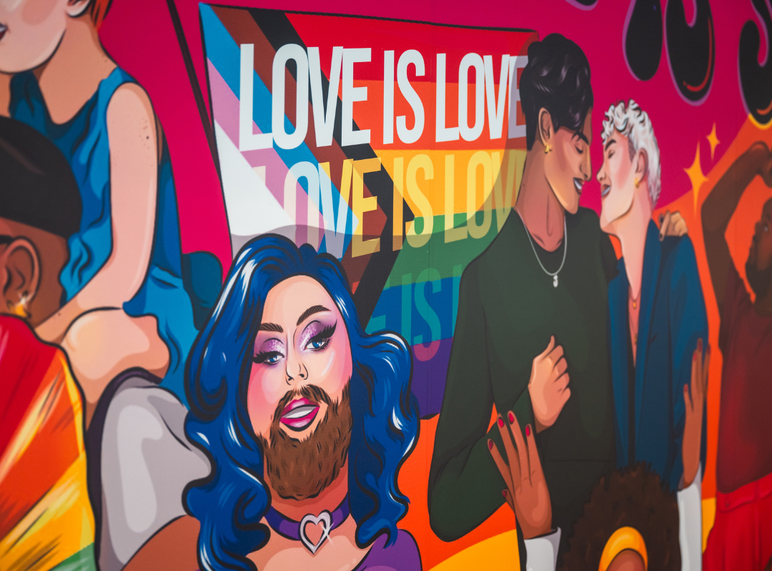 Colourful mural celebrating LGBTQ+ pride with diverse characters, a "Love is Love" message, and a pride flag background.