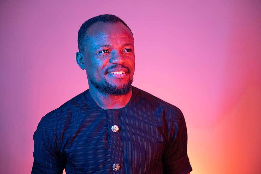 A photograph of Abiola Fasipe wearing a dark navy shirt, lit up by red and blue lights