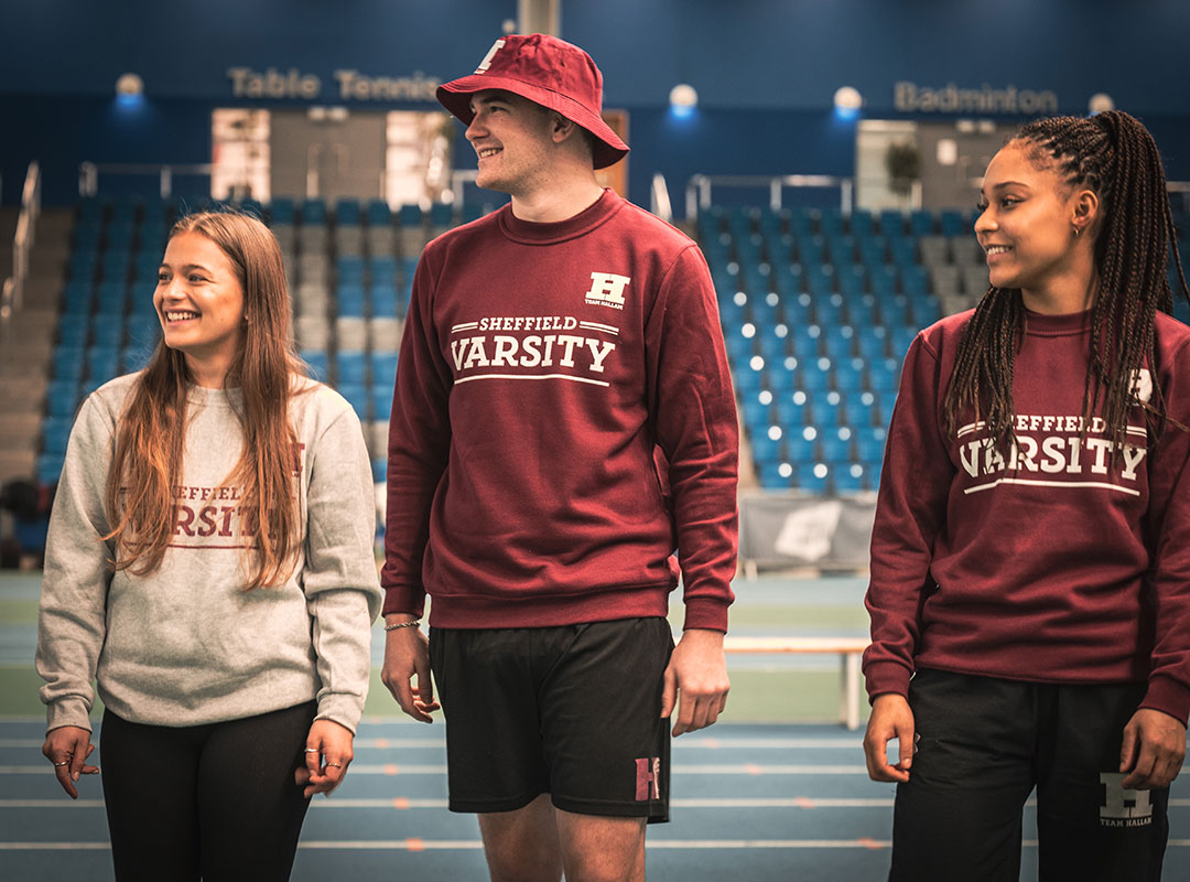 Three students wearing Hallam merch walking, looking to the side, and smiling.