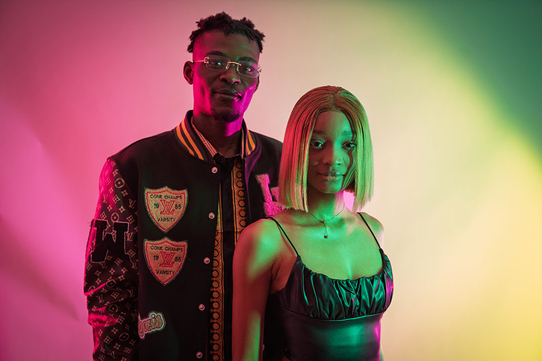 Two students looking at the camera, backlit with bright pink and green lights.