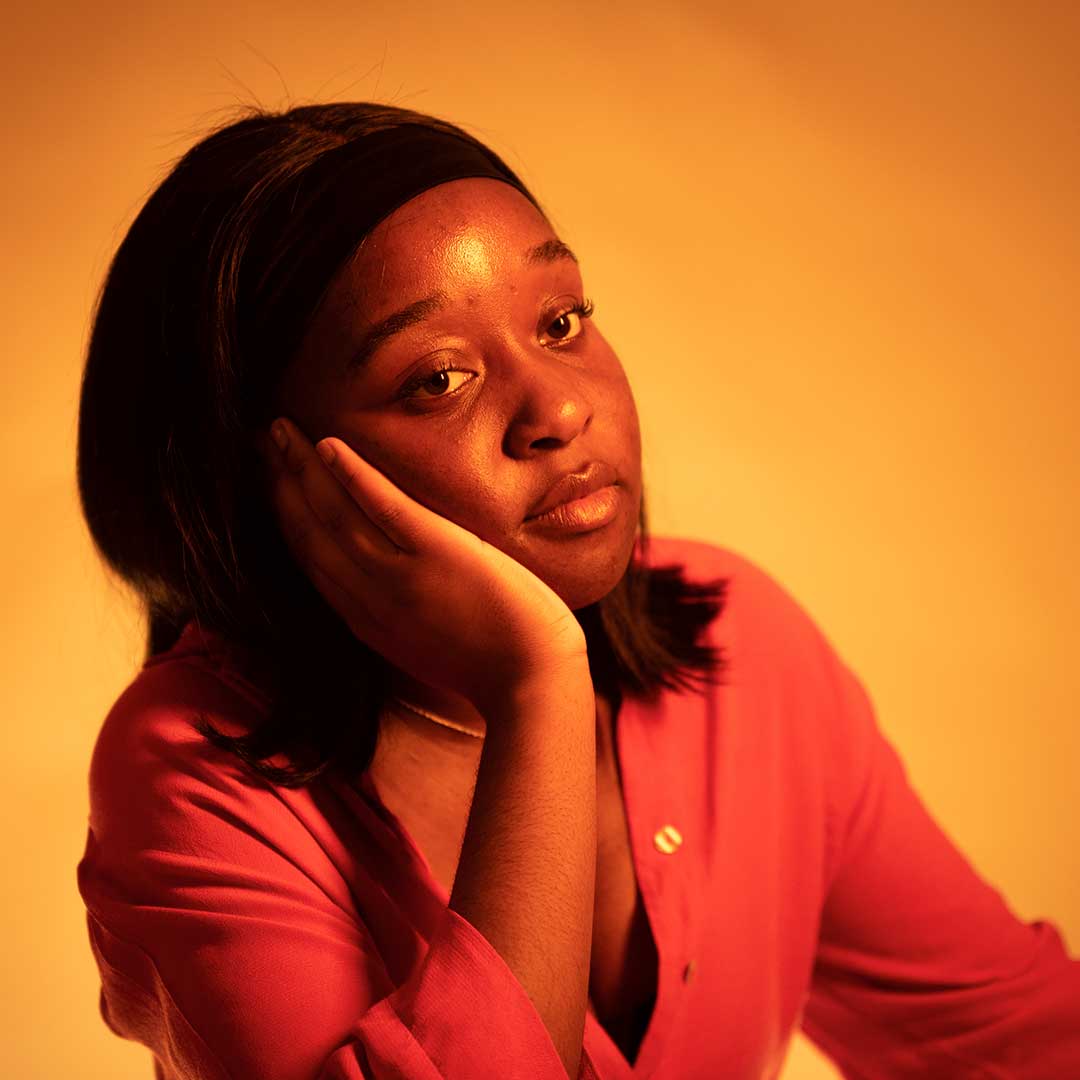 A student against an orange background resting their face on their palm