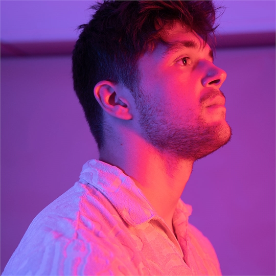 A male student looking up above the camera, lit up by pink lights
