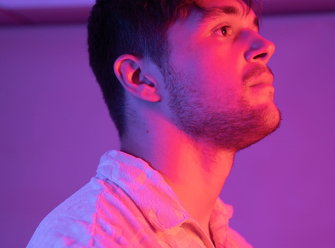 A male student looking up above the camera, lit up by pink lights