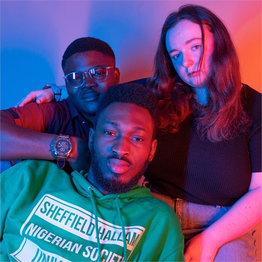 Three students looking into the camera, one is wearing a hoodie that reads 'Sheffield Nigerian Society'