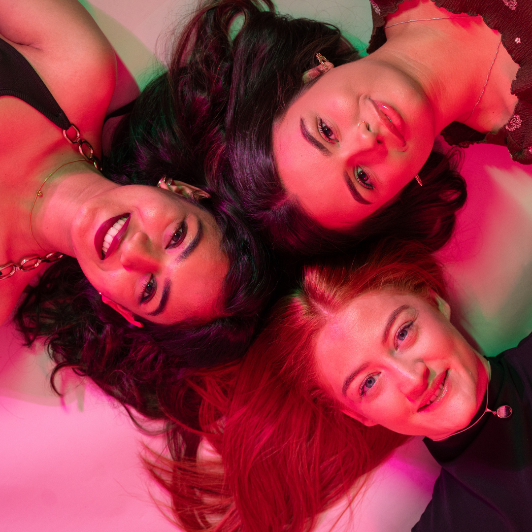 Three students smiling with pink background