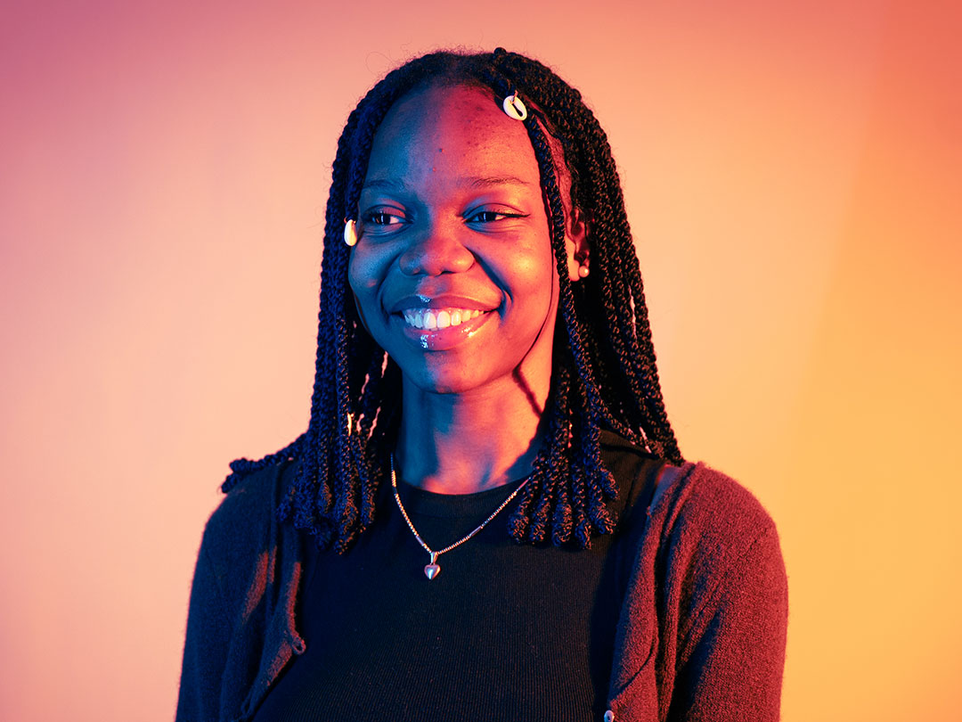 Student smiling at the camera, lit up by neon orange lights