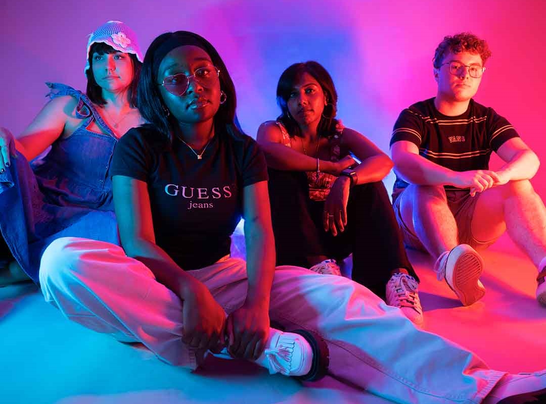Four students sat on the floor lit up by pink and purple lighting