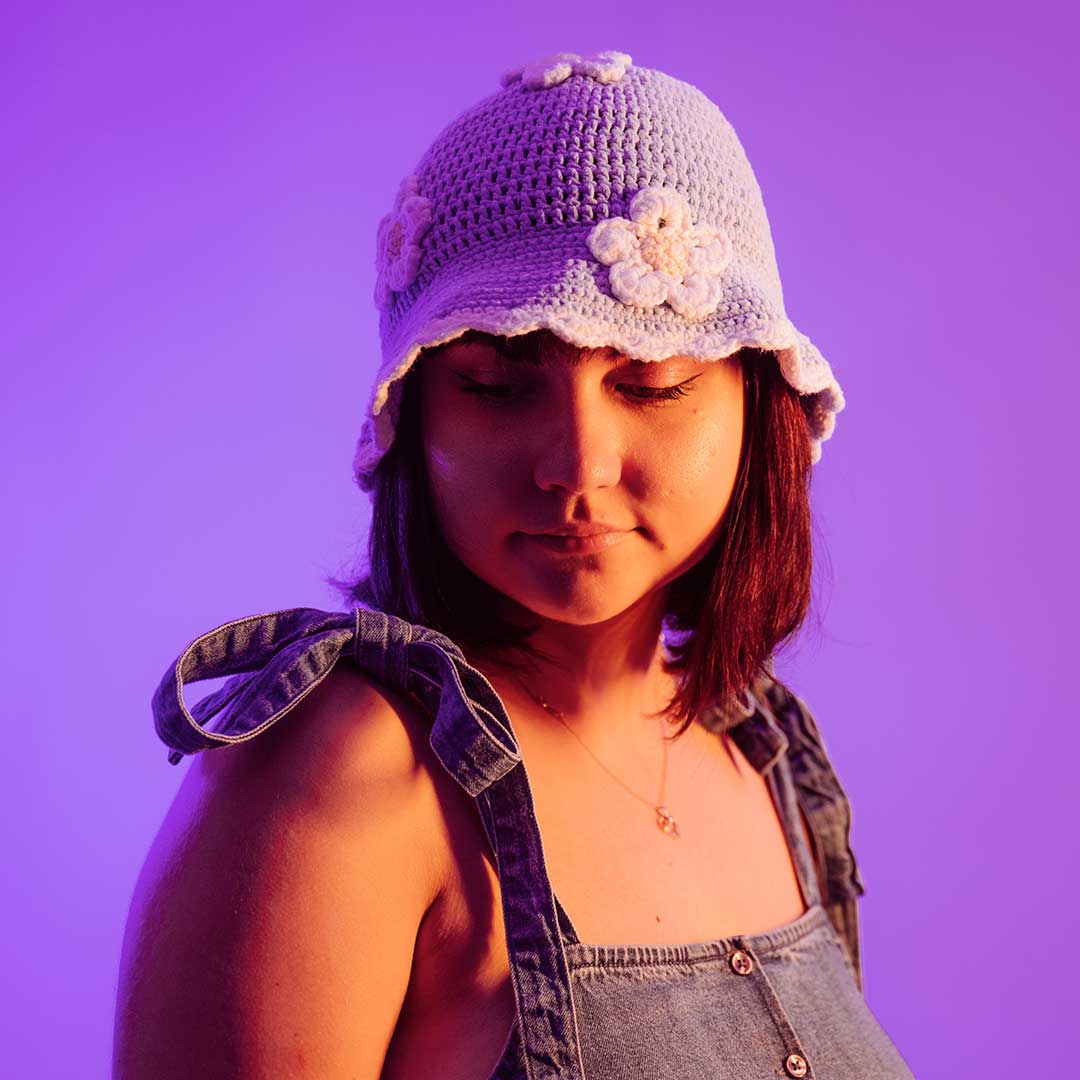 A student wearing a knitted hat with daisies on, the background is lit up with purple neon lights