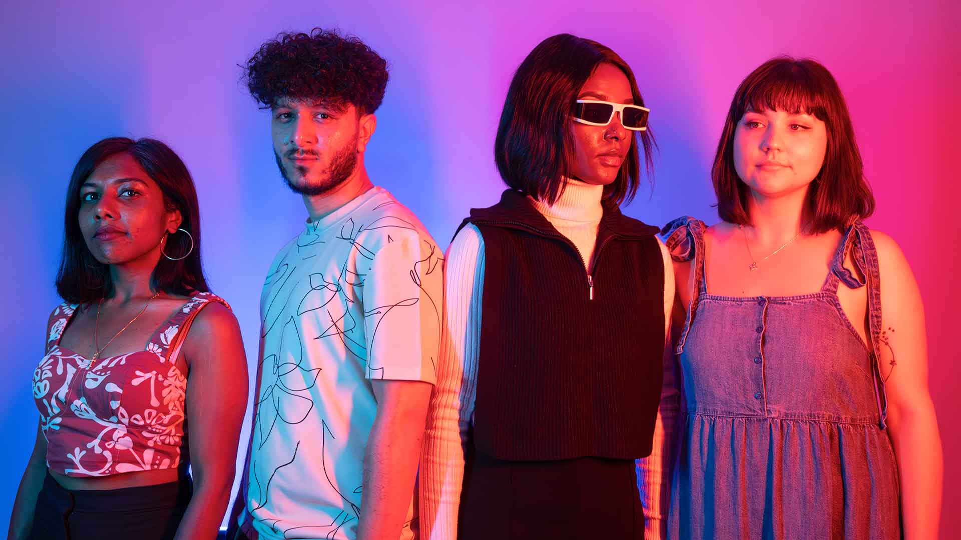 Four students leaning against a wall illuminated by neon lights