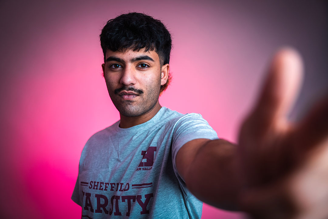 A student, backlit with pink lights, looking at the camera with their hand reaching out.