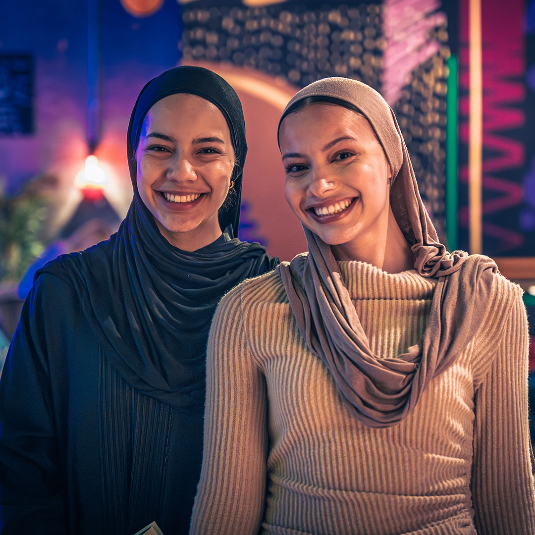 Two students smiling at the camera in front of a vivid, colourful background.